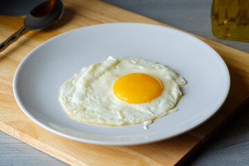 The fried egg is in a white round dish placed on a cutting board