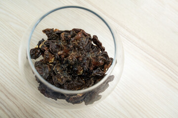 The dark pieces of dry food in glass jar on the light wooden table.