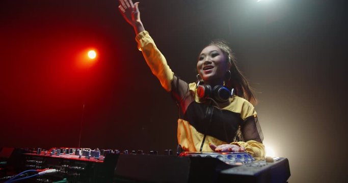Asian female disc jockey working at controller, professional dj doing a live performance in a nightclub with red and blue lights - nightlife, party concept 4k footage