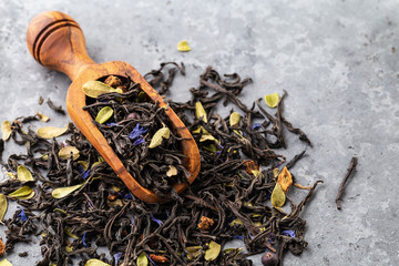 Dry black tea mixed with herbs, flower petals and berries on gray background.