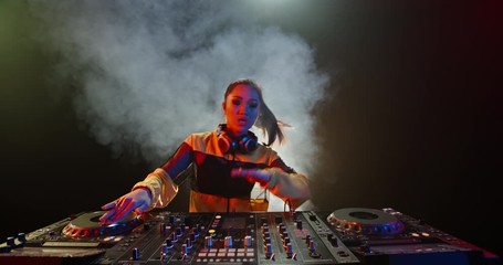Asian female disc jockey working at controller, professional dj doing a live performance in a nightclub with red and blue lights - nightlife, party concept 4k footage