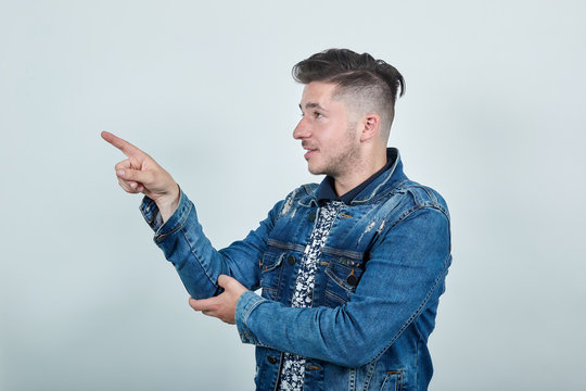 Handsome man in fashion denim jacket pointing on side, space for advertising isolated on gray background. People sincere emotions concept Mock up