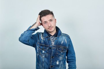 Handsome caucasian young man over isolated gray wall wearing fashion denim jacket clothes keeping hand on head, looking directly