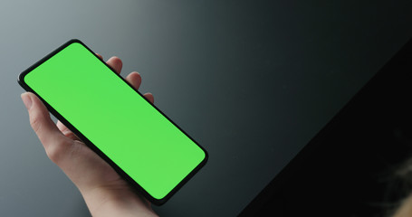 Obraz premium Young woman sitting on a chair near window and using smartphone with green screen