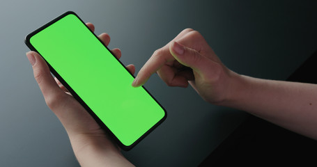 Young woman sitting on a chair near window and using smartphone with green screen