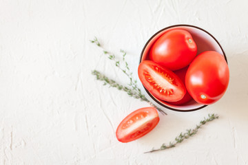 Fresh red, ripe tomatoes in bowl with herbs on a light  background. Juicy tomato vegetables 
