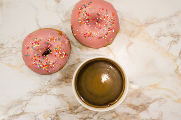 two pink donuts with colorful sprinkles and coffee on a light background. the view from the top. space for your text. the concept of cooking and baking. banner. postcard.