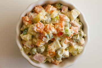 Olivier in a white plate on a pale pink background. the winter salad.ingredients: cucumber, sausage, meat, mayonnaise, sour cream, potatoes, peas, egg. space for your text.