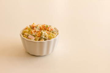 Olivier in a white plate on a pale pink background. the winter salad.ingredients: cucumber, sausage, meat, mayonnaise, sour cream, potatoes, peas, egg. space for your text.
