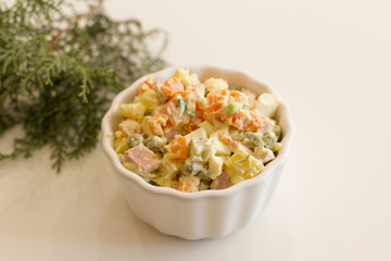Olivier in a white plate on a pale pink background. the winter salad.ingredients: cucumber, sausage, meat, mayonnaise, sour cream, potatoes, peas, egg. space for your text. a dish of salad and a sprig