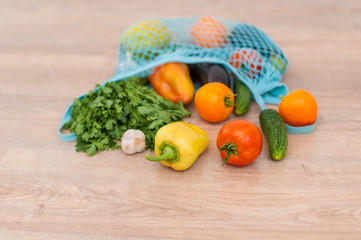 Assortment of organic vegetables in a mesh bag randomly scattered on a wooden surface, top view selective focus