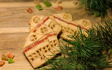 Christmas gingerbread cookies in the form of house on a wooden table surrounded by pine branches and colored candied fruits, flat lay