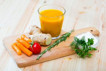 Glass with carrot juice with ginger, greens and vegetables on wooden desk