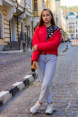 Beautiful teenager girl on a background of a city street in a bright red jacket.