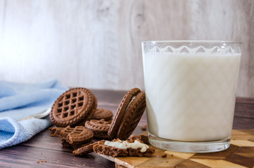 sandwich cookies and a glass of milk on a wooden table.