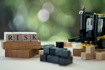 Miniature businessman sitting on forklift with wooden word RISK.  Concept of risk assessment
