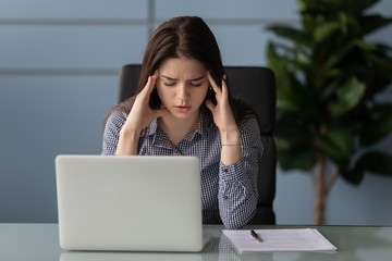 Tired female employee suffer from strong migraine at workplace