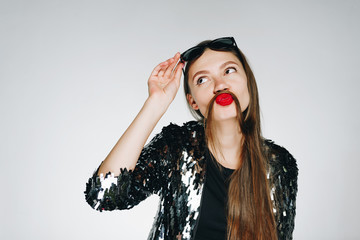a bright stylish girl with red lipstick jokingly put her hair on her upper lip, depicting a...
