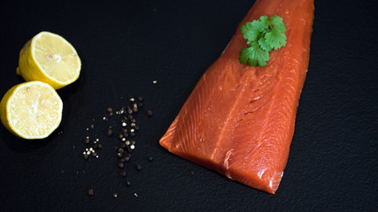 Fresh raw salmon fish steak with spices on ice over dark stone background