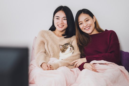Young beautiful Asian women lesbian couple lover watching television on the bed with the cat together in bed room at home with smiling face.Concept of LGBT sexuality with happy lifestyle together.
