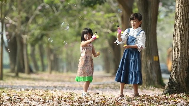 Two brothers little asian lovely girl blowing soap bubbles and laughing in summer public park.Outdoors at the daytime with bright sunlight. Loving and happy family Asian girl chasing soap bubble. 