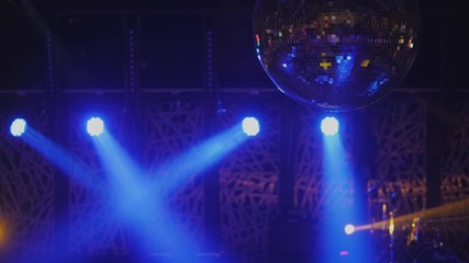 Glittering disco ball against the background of spotlights. Concert spotlights on stage. Dance floor and light music in the nightclub.