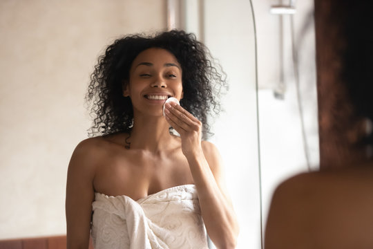 Smiling african American woman do facial treatment in bathroom
