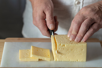 A man cuts  hard cheese with a ceramic knife on a marble cutting board in the kitchen.