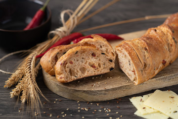 Sliced rye-wheat baguette with bran and pepperoni on a wooden board. Three slices of cheese, pepperoni and ears of rye und wheat.