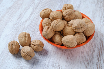Walnuts in a bamboo bowl on a white wooden board.