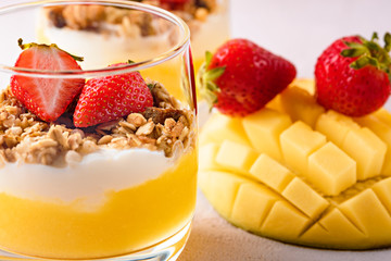 dessert with ricotta cheese, mango, granola and strawberries on pink background.