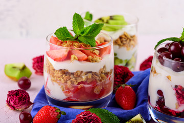 healthy dessert with cherries, strawberries, kiwi, cream cheese ricotta, granola, mint in glass on blue napkin on light pink background