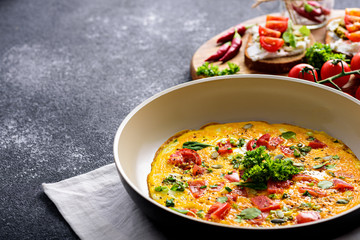 crop scrambled eggs with tomatoes, spinach and pumpkin seeds in frying pan with toast with cottage cheese, pesto sauce, chili and cherry tomatoes on black background