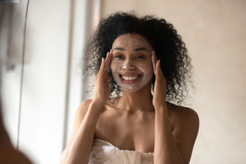 Smiling biracial woman do morning skincare treatment in bathroom