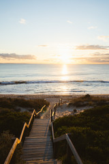 Sandy, beach staircase down to the sea through the sand dunes with a beautiful sunset over the ocean and waves at Cottesloe, Perth, Western Australia. 
