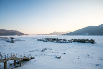 Winter Scenery of Sunset on the Lake Songhua against snow mountains and frozen lake with fog on the lake surface, Jilin Province, China