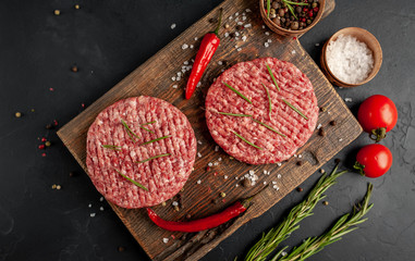 Raw beef burger cutlets with herbs and spices on a concrete background