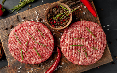 Raw beef burger cutlets with herbs and spices on a concrete background