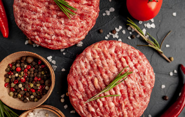 Raw beef burger cutlets with herbs and spices on a concrete background