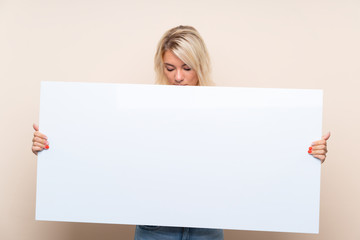 Young blonde woman over isolated background holding an empty white placard for insert a concept