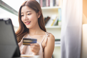 Happy Asian young woman doing online shopping at home.She holding credit card and using laptop computer.Smiling asian woman on couch using tablet to shop online n the living room.