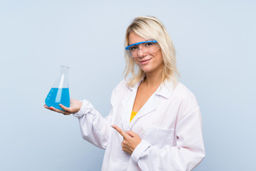 Young blonde woman over isolated background with a scientific test tube and pointing it