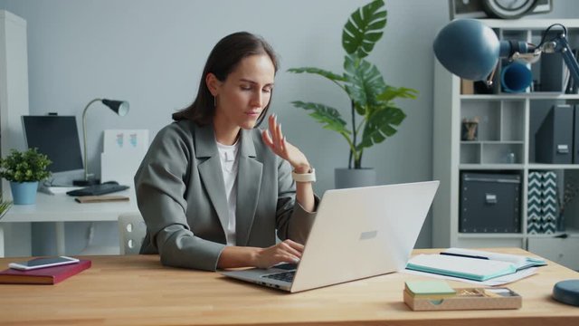 Exhausted employee pretty young woman is using laptop then touching head feeling tired and stressed. Hard-working people and stressful work concept.