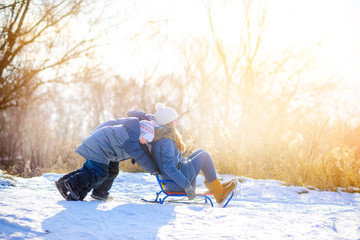 Happy children play in a snowy winter park at sunset. Sledding and having fun. Winter fun. Holidays.