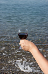 a glass of red wine in his hand. Waves and sea in the background