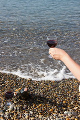 a glass of red wine in his hand. Waves and sea in the background