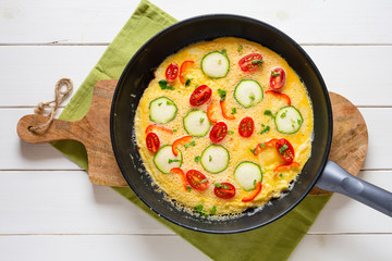 Omelette with zucchini, lamb's lettuce, tomatoes and red pepper in a pan. Frittata - italian omelet. Flat lay