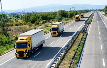 Caravan or convoy of Four yellow Lorry Lorry trucks in line on a country highway under a beautiful...