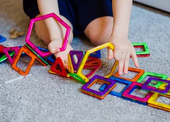 Fototapete Lego Kid plays with a magnetic constructor toy. A little child girl is playing with colorful blocks. Close up. Girl  playing intellectual toys. Children's magnetic designer for development of motor skills.  © Julia
