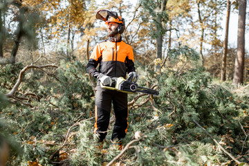 Full length portrait of a professional lumberman in protective workwear logging with chainsaw in the pine forest